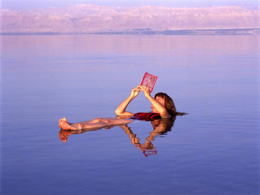 Person floating in the Dead Sea while reading a book, showcasing the unique buoyancy of this salt-rich lake.