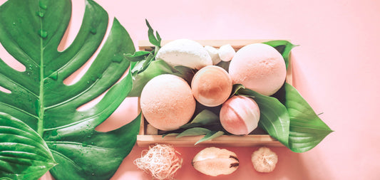 DIY: Pink Himalayan Salt Bath Bomb Recipe with colorful bath bombs arranged in a wooden tray surrounded by green leaves.